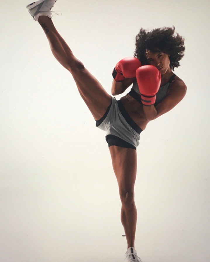Ein weibliches Model mit roten Boxhandschuhen kickt mit ihrem rechten Bein in die Luft.