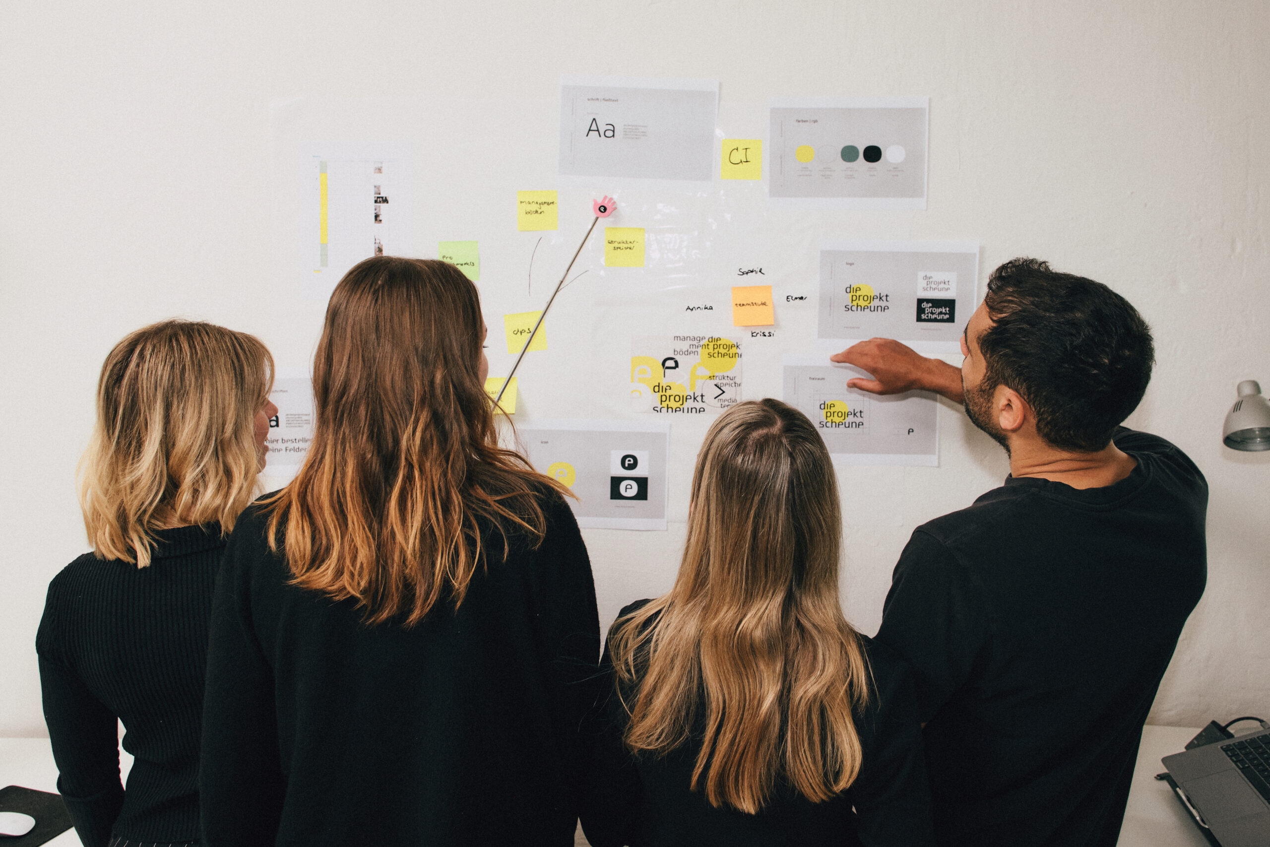 Team-die-projektscheune-4 Das Team ist von hinten zu sehen, wie sie vor dem Whiteboard stehen.
