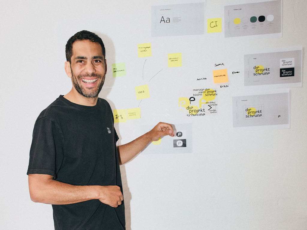Elmar-die-projektscheune Zu sehen ist der Geschäftsführer Elmar Burke, wie er vor dem Whiteboard steht und lacht.