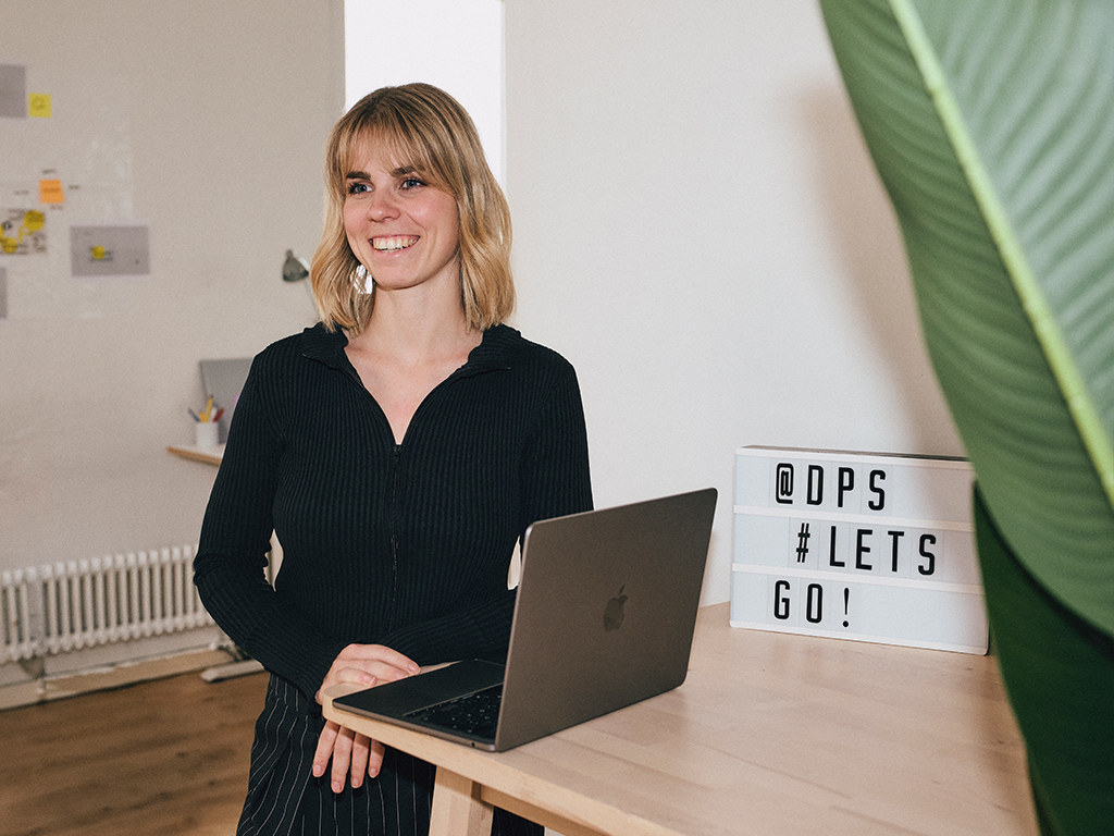 Krissi-die-projektscheune Zu sehen ist Model-Managerin und -Bookerin Ann-Kristin Seiter, wie sie mit ihrem Laptop an einem Hochtisch steht.